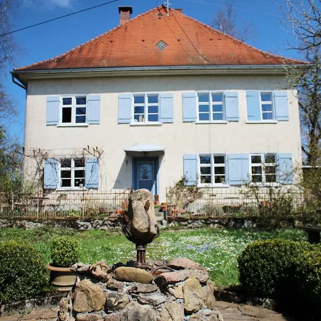 Ein eleganter Steinbrunnen steht vor einem gemütlichen Haus, umgeben von einer einladenden Gartenlandschaft.