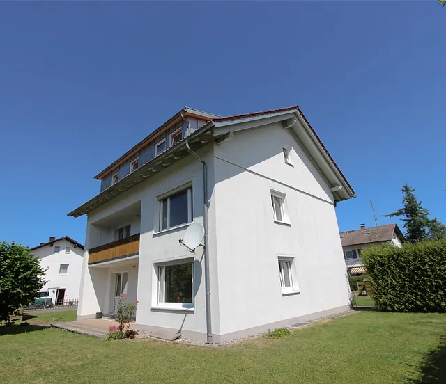 Zweistöckiges weißes Haus mit Satteldach und Garten mit Rasen und Hecke