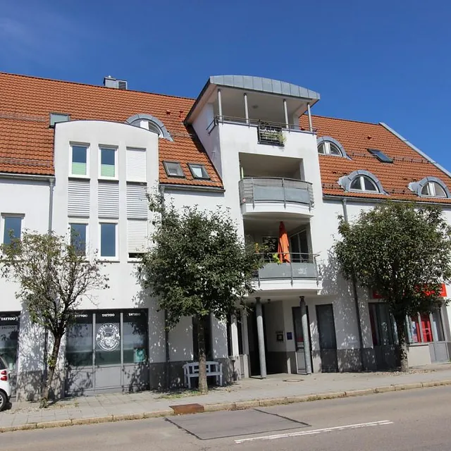 Weißes Gebäude mit einem Auto, das davor geparkt ist, vor einem klaren Himmel.