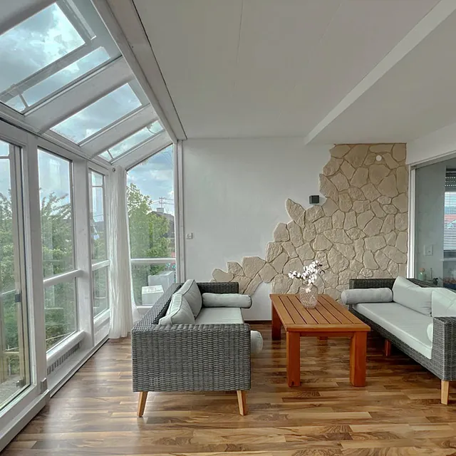 Wohnzimmer mit zwei grauen Sofas, einem Holztisch und großen Glasfenstern mit Blick ins Grüne