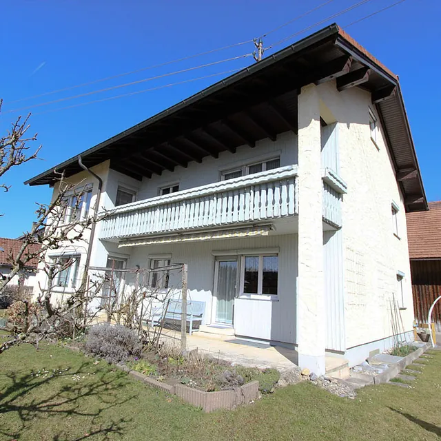 Zweistöckiges weißes Haus mit Balkon und Garten im Vordergrund