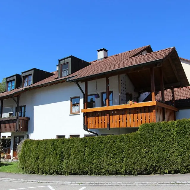 Ein Haus mit einem Balkon und einer grünen Hecke.