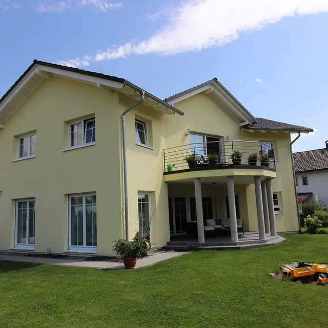 Gelbes Haus mit Balkon und gepflegtem Rasen, umgeben von einer einladenden Atmosphäre.
