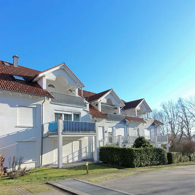 Reihenhaus mit weißen Fassaden, roten Ziegeldächern und Balkonen unter klarem blauem Himmel