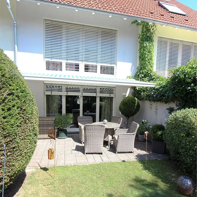 Reihenhaus mit Terrasse, Gartenmöbeln und gepflegtem Garten mit Sträuchern und Kletterpflanzen am Haus