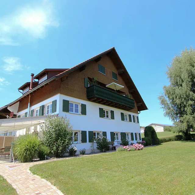 Großes weißes Holzhaus mit grünem Balkon und Wintergarten auf gepflegtem Rasen unter blauem Himmel