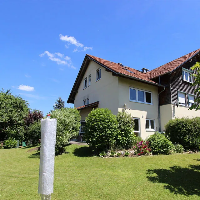 Zweistöckiges Wohnhaus mit rotem Satteldach und gepflegtem Garten bei sonnigem Himmel