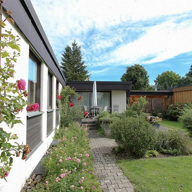 Einfamilienhaus mit großem Garten, Terrasse mit Tisch und Stühlen, umgeben von Blumen und Sträuchern