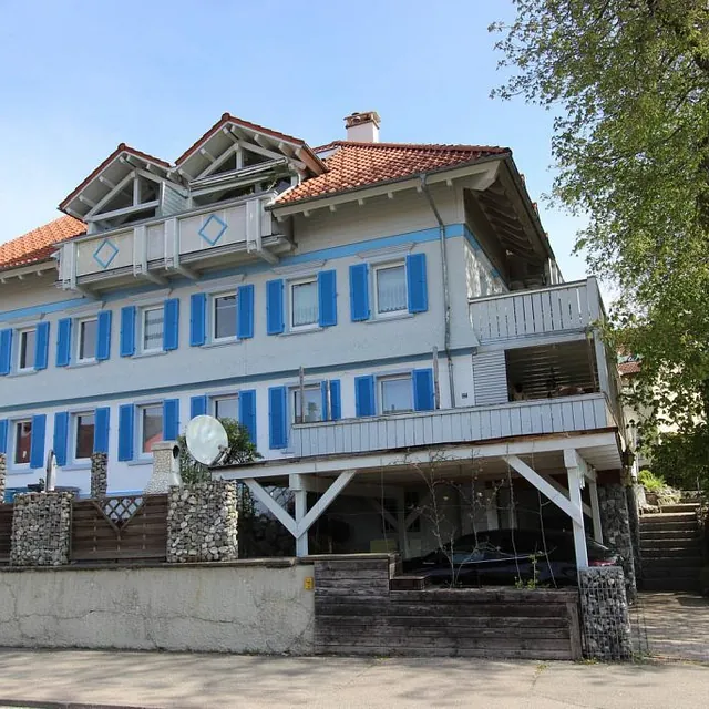Ein charmantes Haus mit blauen Fensterläden und einem weißen Dach, das einladend in der Sonne strahlt.